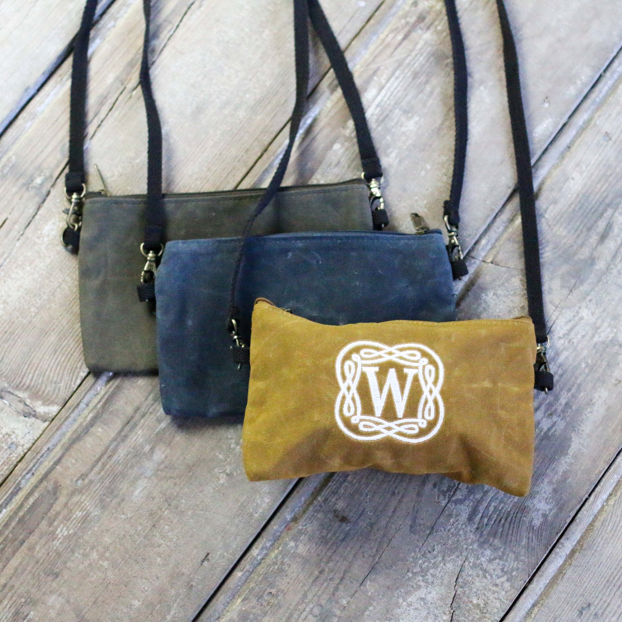 Waxed canvas crossbody clutch with customized initials being worn by a person