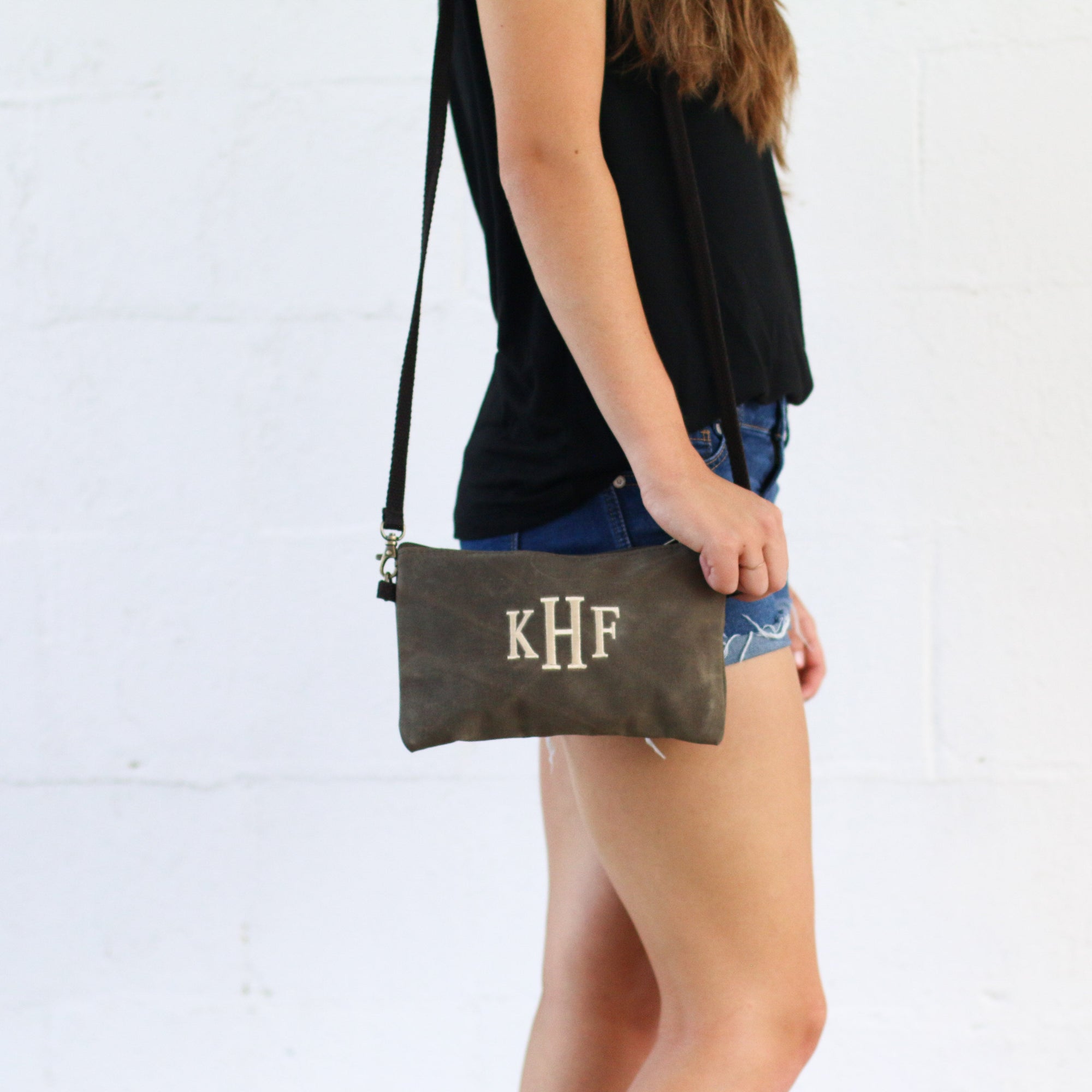 Waxed canvas crossbody clutch with customized initials being worn by a person